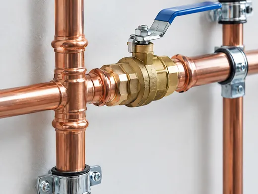 Kupferleitungen mit Pressverbindern und Kugelhahn an einer weißen Wand